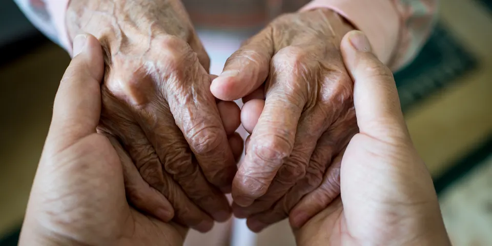 Primer plano de las manos de una persona mayor sostenidas en señal de apoyo, que simbolizan el cuidado y la compasión ante el Alzheimer.