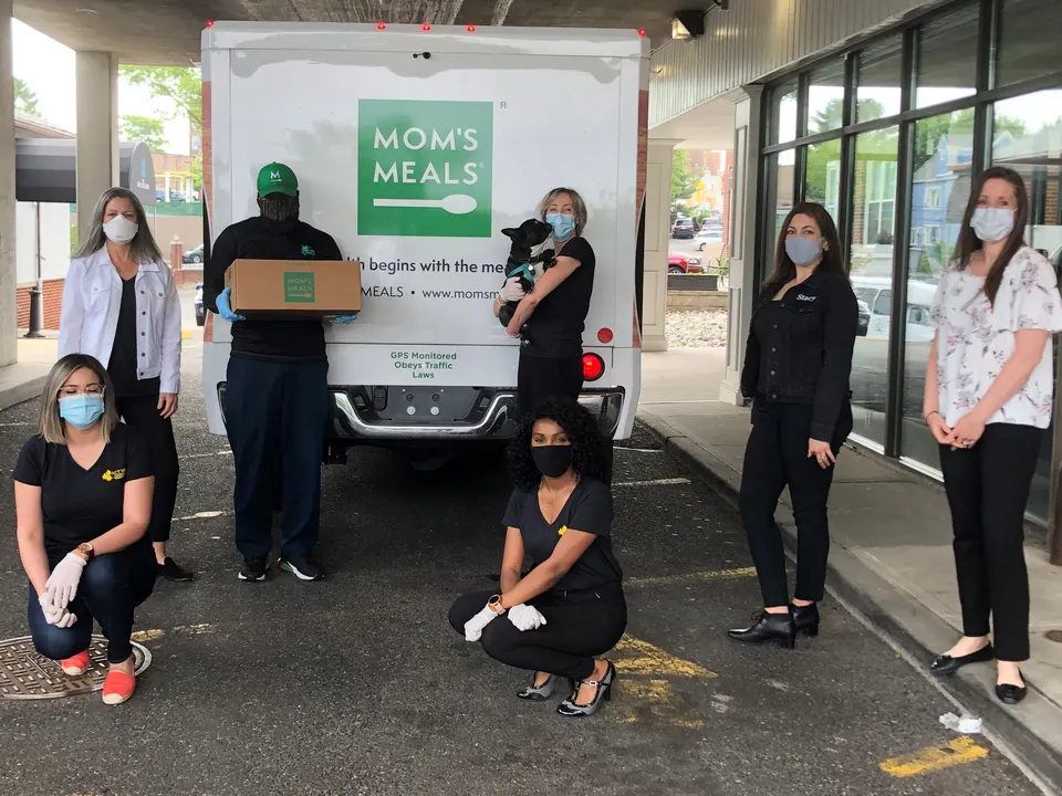 Equipo de Act Now Foundation posando junto a un camión de Moms Meals entregando comidas a personas mayores durante la pandemia